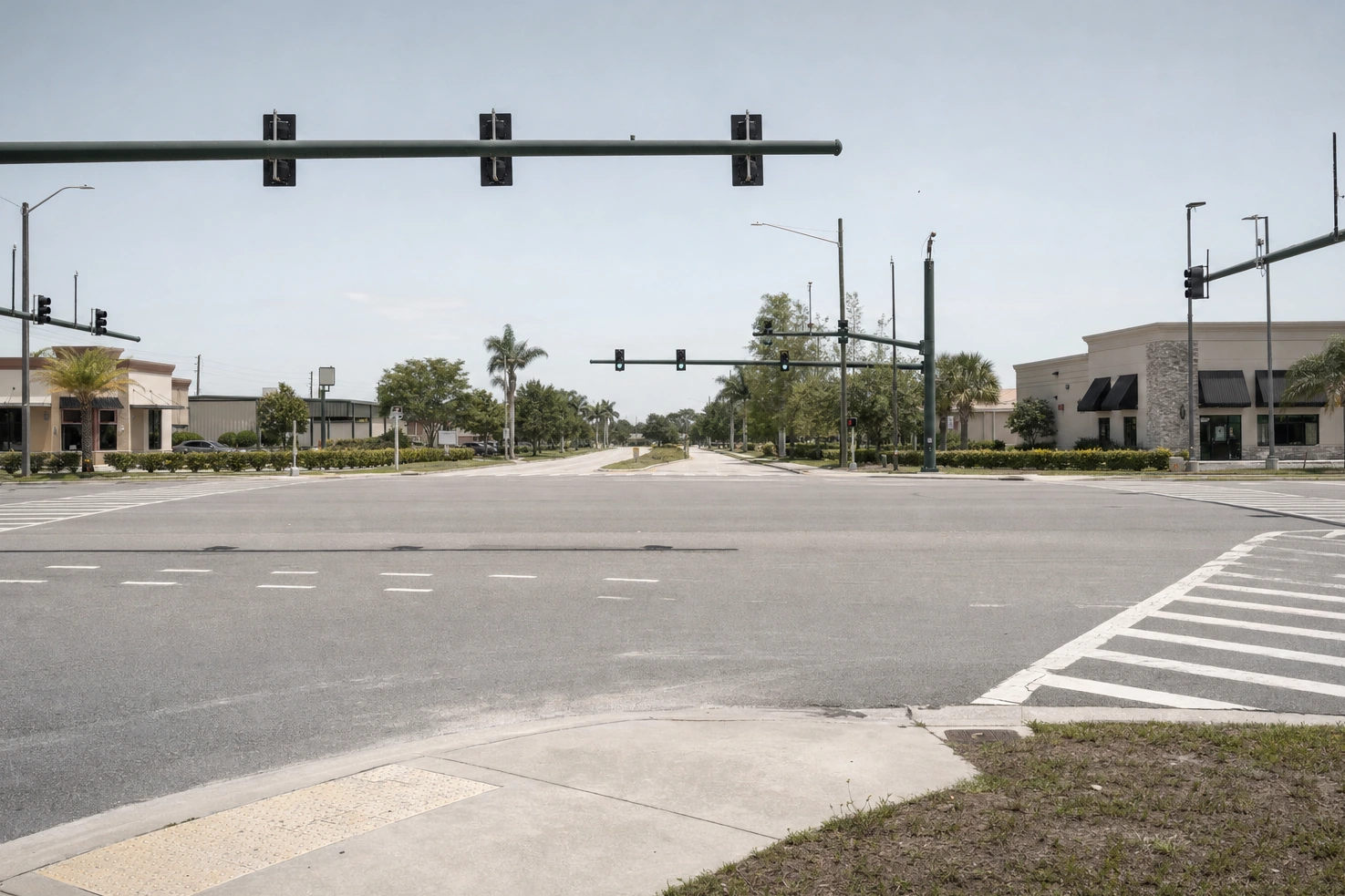 A wide suburban intersection we photographed square-on at midday — signal gantries overhead, empty crosswalks, low buildings on all four corners.