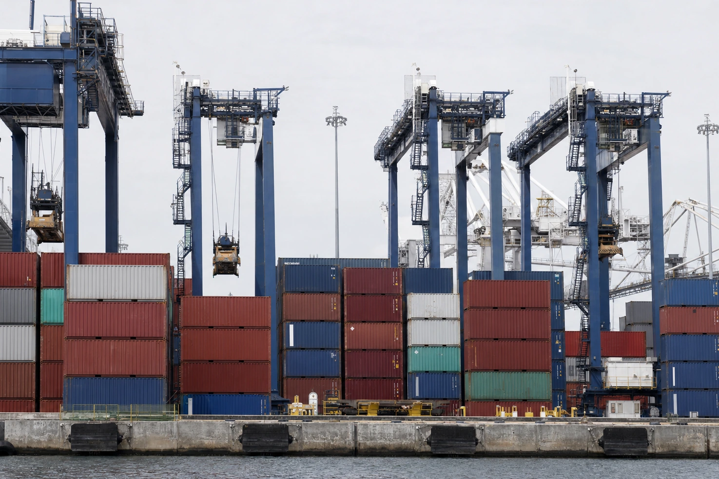 Container stacks and gantry cranes at a working port, photographed by us square-on at midday under flat light.