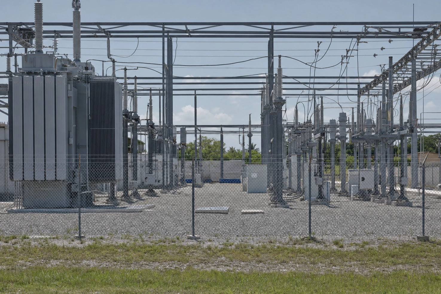 An electrical substation behind a chain-link fence, photographed by us at midday — transformers and gantries in flat light.