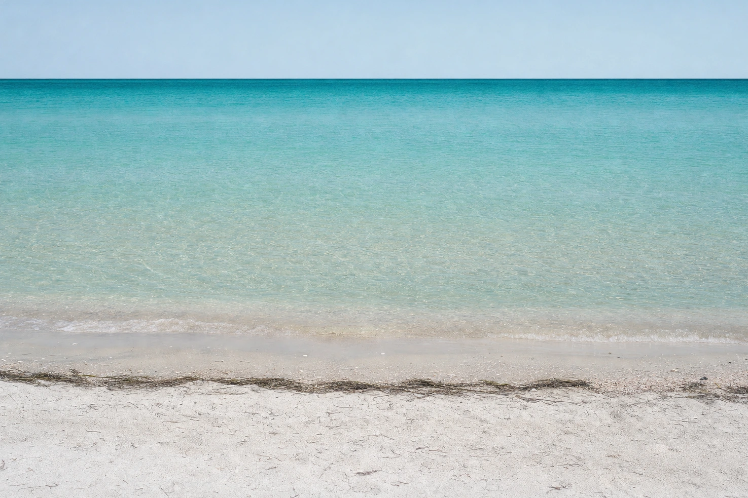 A shoreline of pale sand and turquoise shallows we photographed straight on at midday, horizon level, nobody in the frame.