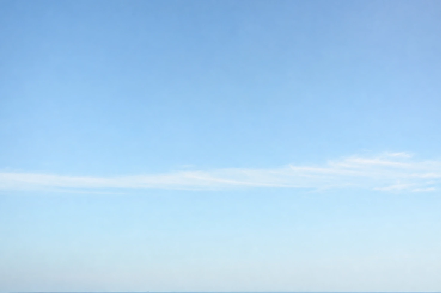An almost featureless bright sky we photographed with a single thin band of cloud and the horizon at the very bottom of the frame.