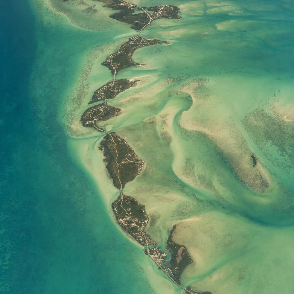 Our high-altitude photograph of a chain of low islands lying in turquoise shallows at midday.