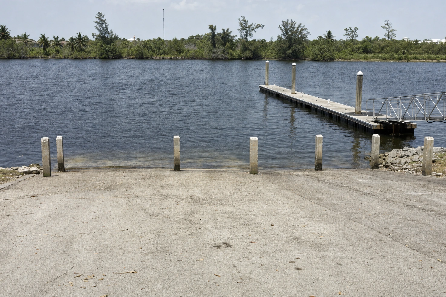 A concrete boat ramp meeting dark water, photographed by us at midday: bollards, a floating dock, flat even light.